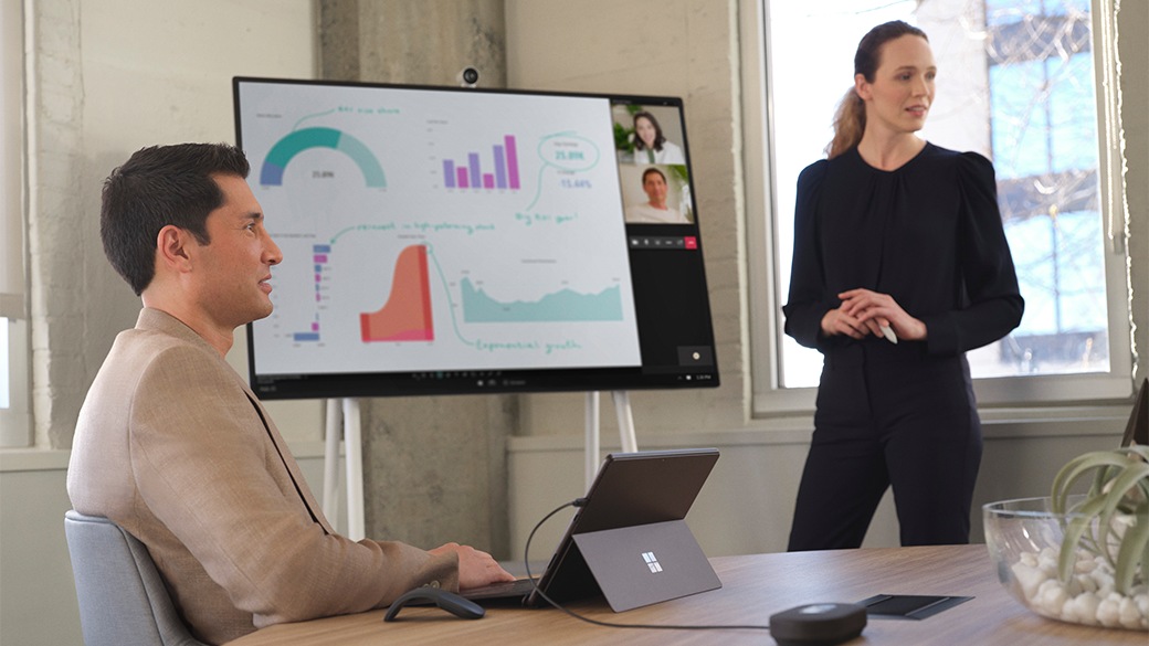 Two people in a conference room using Surface Pro 8 for Business and Surface Hub 2S.