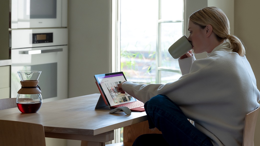 机にデスクに座り、法人向け Surface Pro 7+ で作業をしている人物。