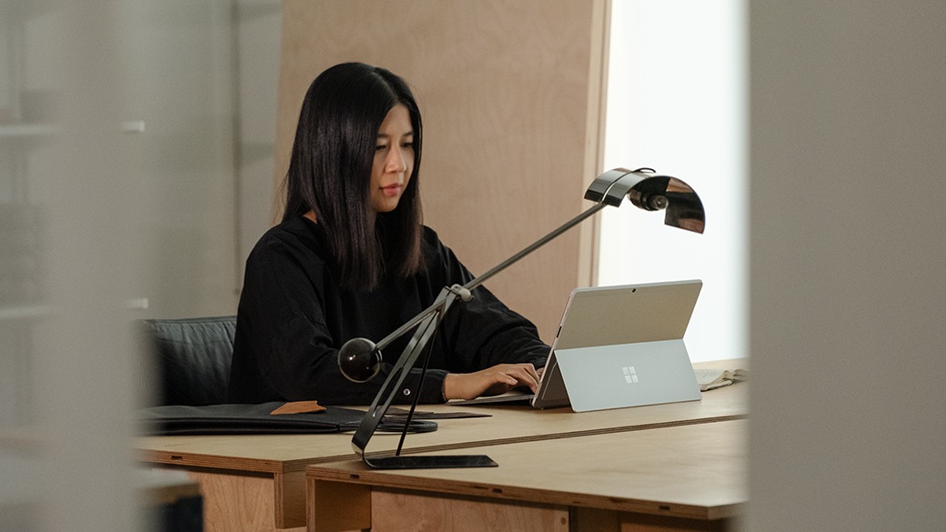 Pöydän ääressä istuva henkilö katsoo Surface Pro X yrityksille -laitteen näyttöä, jossa näkyy Teams-puhelu.