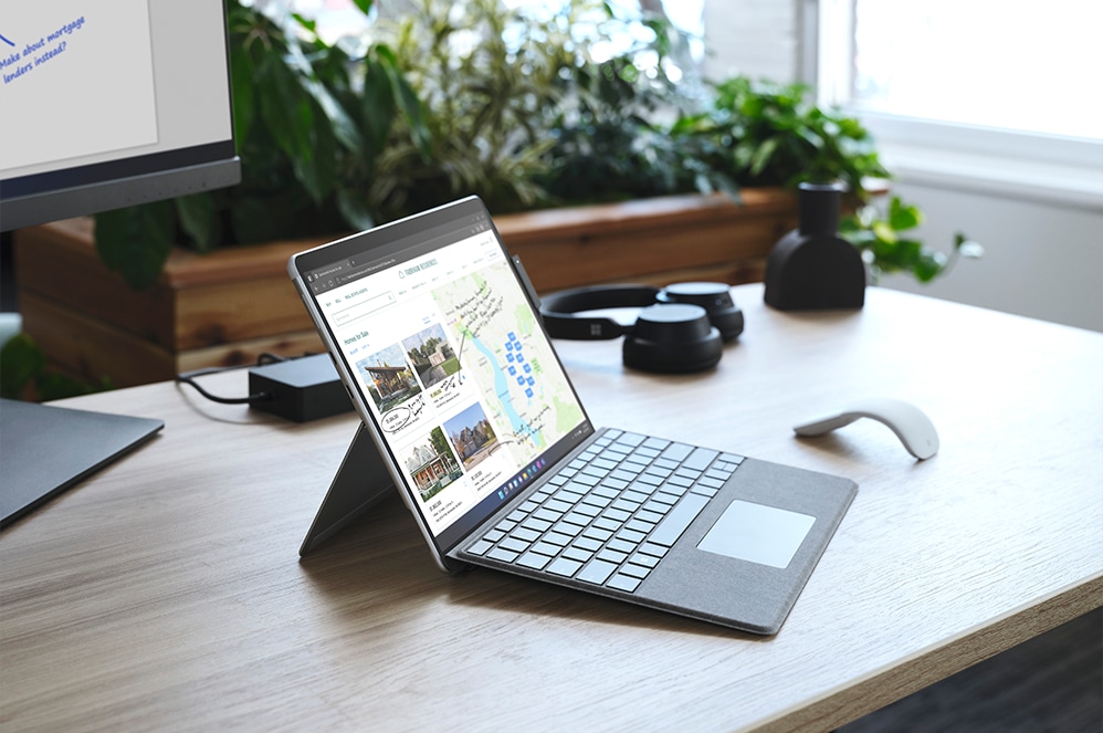 Surface Pro X til erhverv på et skrivebord opstillet på dens kickstand med et Type Cover fastgjort.