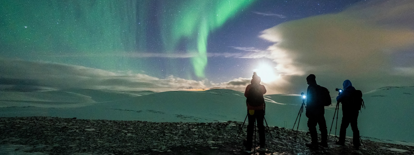 Three people with cameras photographing the northern lights on a cold winter night in Northern Norway.