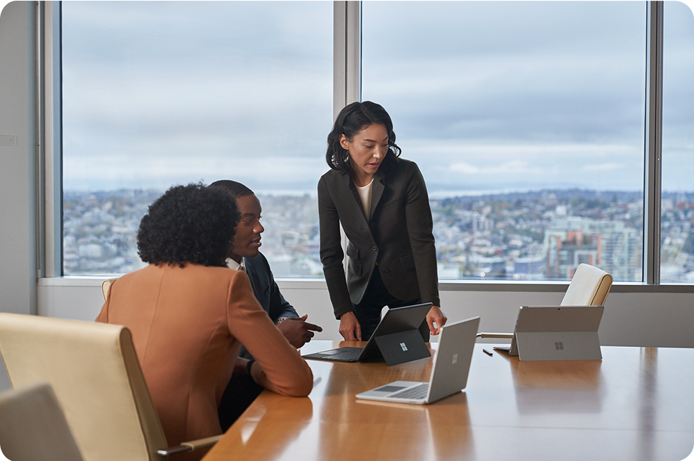 Tre kolleger ses i et kontormiljø. Surface Pro- og Laptop Go 2-enheder står på et konferencebord.