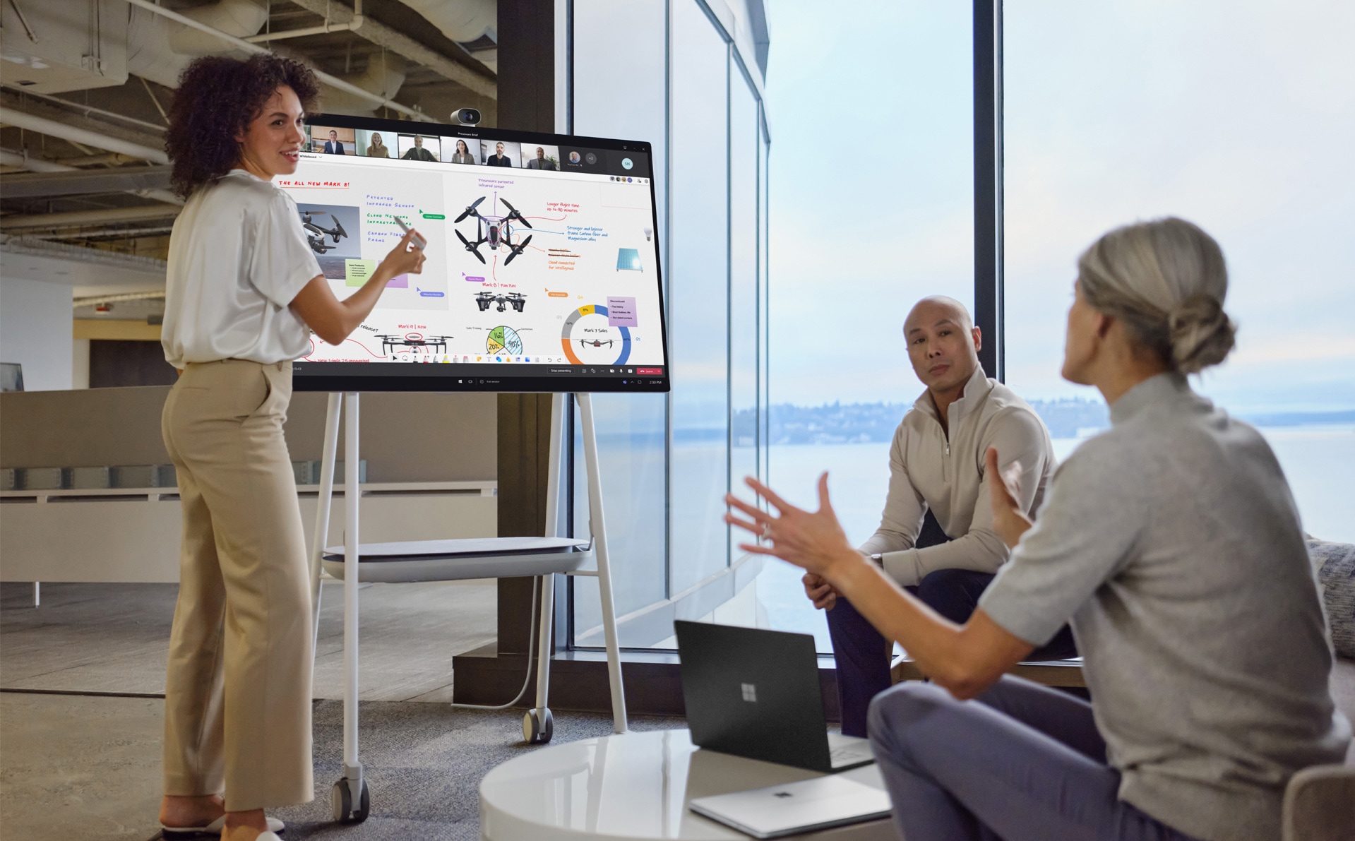 Colegi de muncă prezenți fizic interacționează cu o prezentare PowerPoint în Teams, în timp ce colegii care lucrează de la distanță observă