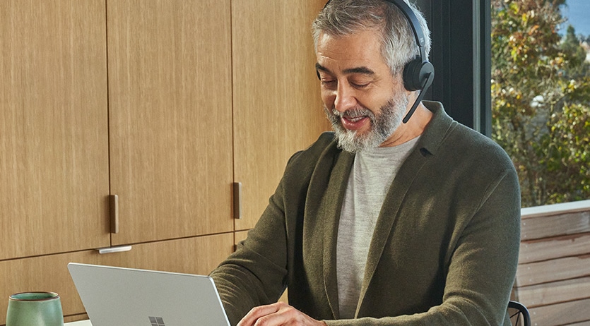 Una persona que trabaja desde casa con Surface Laptop Go 2 mientras lleva puestos unos Microsoft Cascos inalámbricos modernos