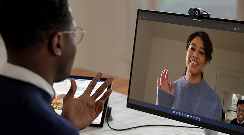 男人使用連接到外接螢幕的 Surface 裝置和 Microsoft 時尚網路攝影機，在 Microsoft Teams 通話中與同事交談