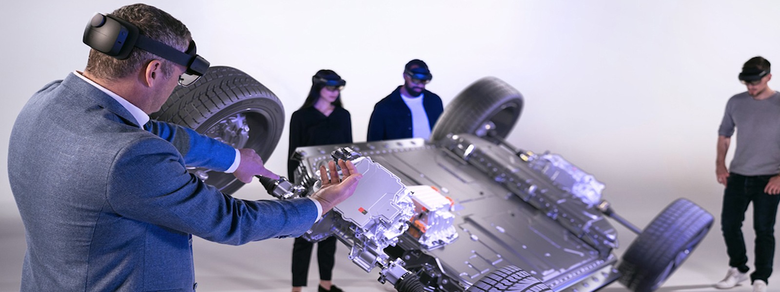 Four people using HoloLens 2 devices to view an AR model of the base of a car.