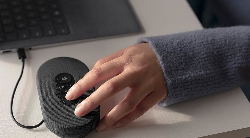En persons hand kan ses hantera en Microsoft USB-C-högtalare för att initiera ett Microsoft Teams-samtal