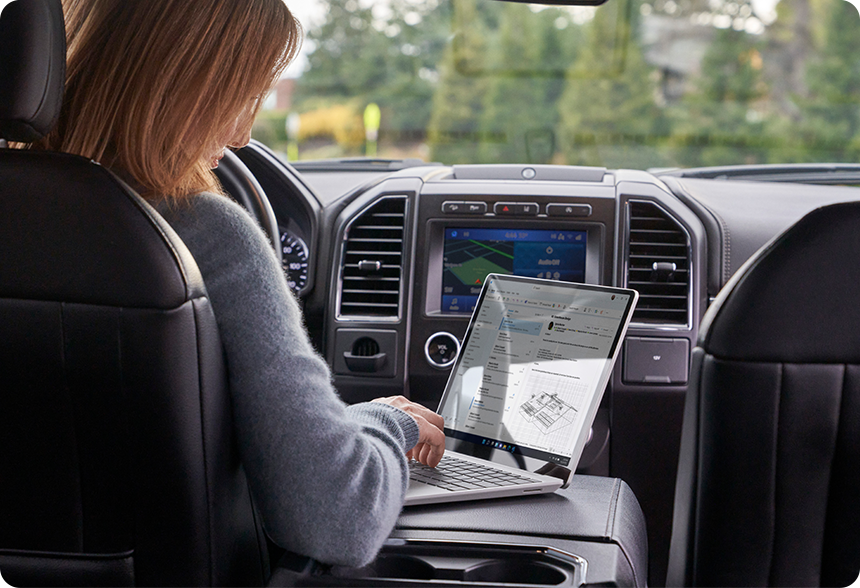 Een persoon gebruikt een Surface Laptop Go 2-apparaat, al zittend in een voertuig