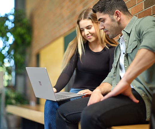 Δύο άτομα παρατηρούν την οθόνη ενός Surface Laptop Go 2 σε γραφείο