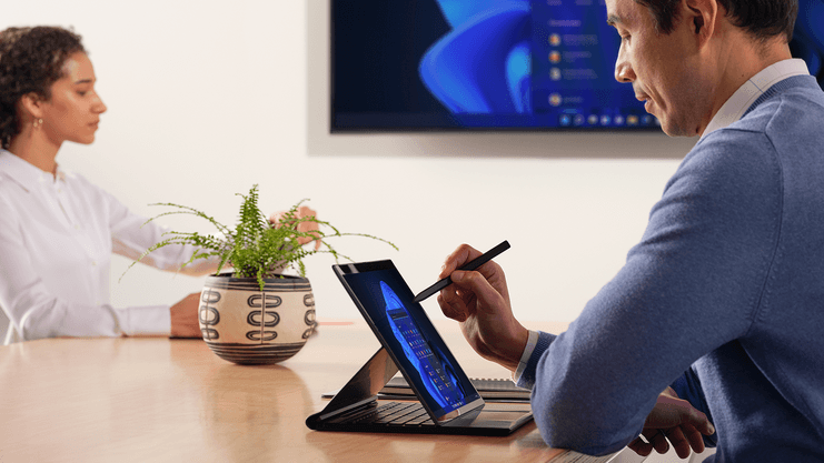 Two people at a table looking at a Windows 11 device and screen.