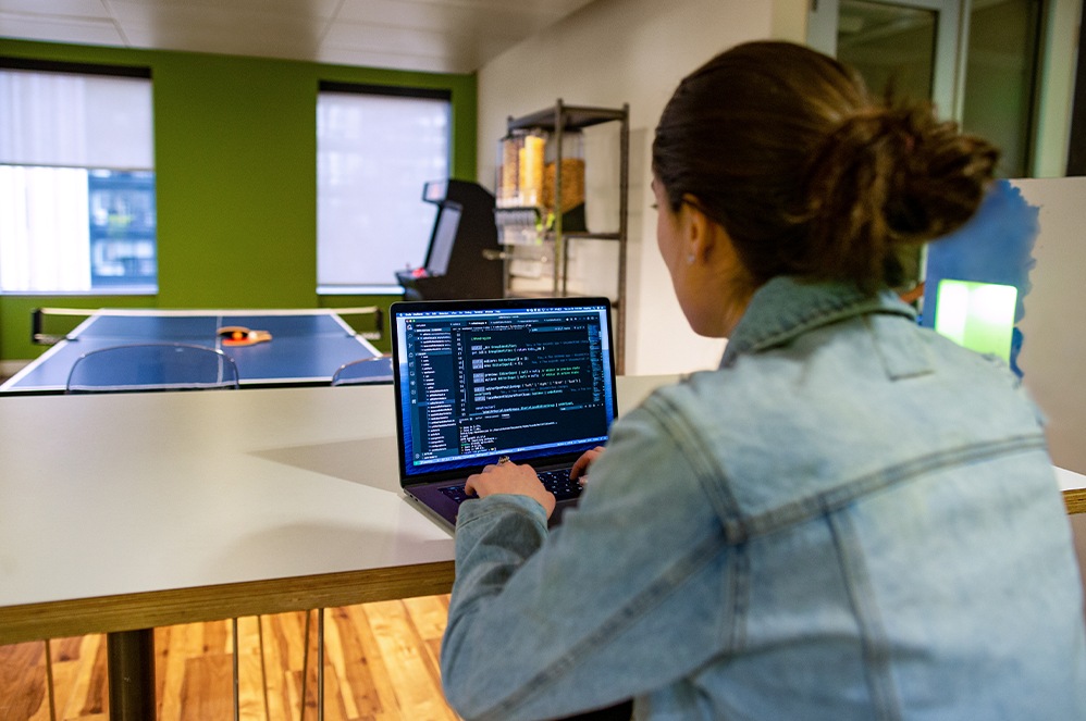 A person reviews code on a laptop while sitting near a ping pong table.