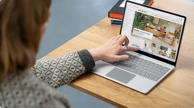 A woman touches her screen on Surface Laptop Go 2 to interact with apps.
