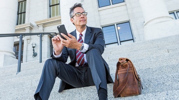 Una persona sentada en los escalones fuera de un edificio usando un teléfono móvil.