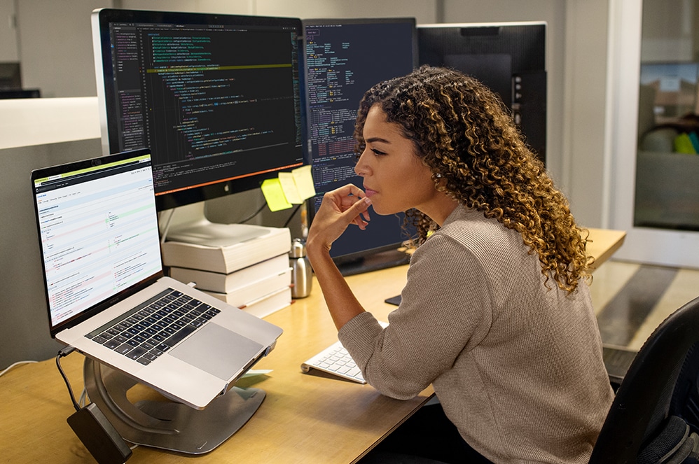 한 개발자가 직장에 있는 세 대의 컴퓨터 모니터에서 Visual Studio를 사용하여 코딩 작업을 합니다.