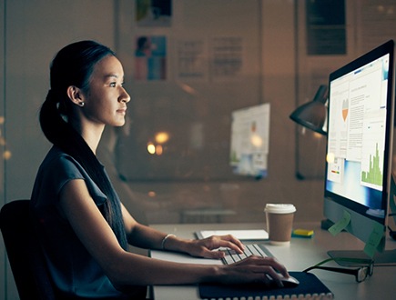En person, der sidder ved et skrivebord og ser på data på en computer.
