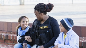 Un agente de policía sentado en un escalón con dos niños riendo.