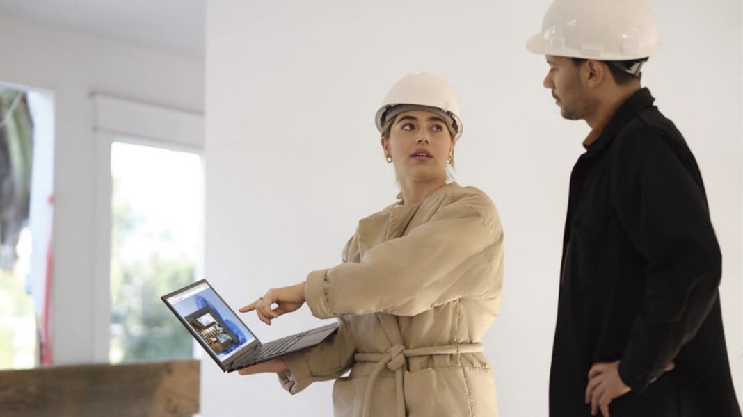 Two people wearing hard hats looking at information on a laptop.