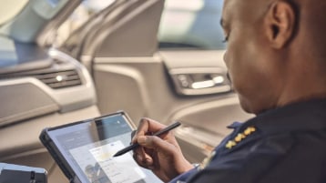 A public safety officer sitting in a car using a tablet and pen.