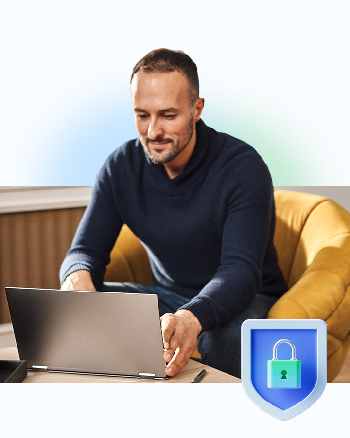 Ein Mann sitzt an einem Laptop mit einem Schutzschild als Symbol für Sicherheit im Vordergrund.