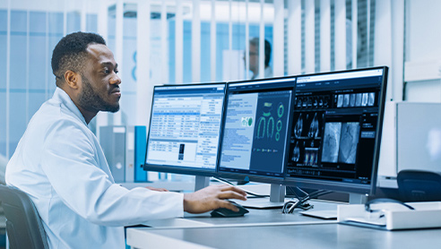 Un operatore del settore sanitario a una scrivania utilizza un computer e osserva tre monitor.