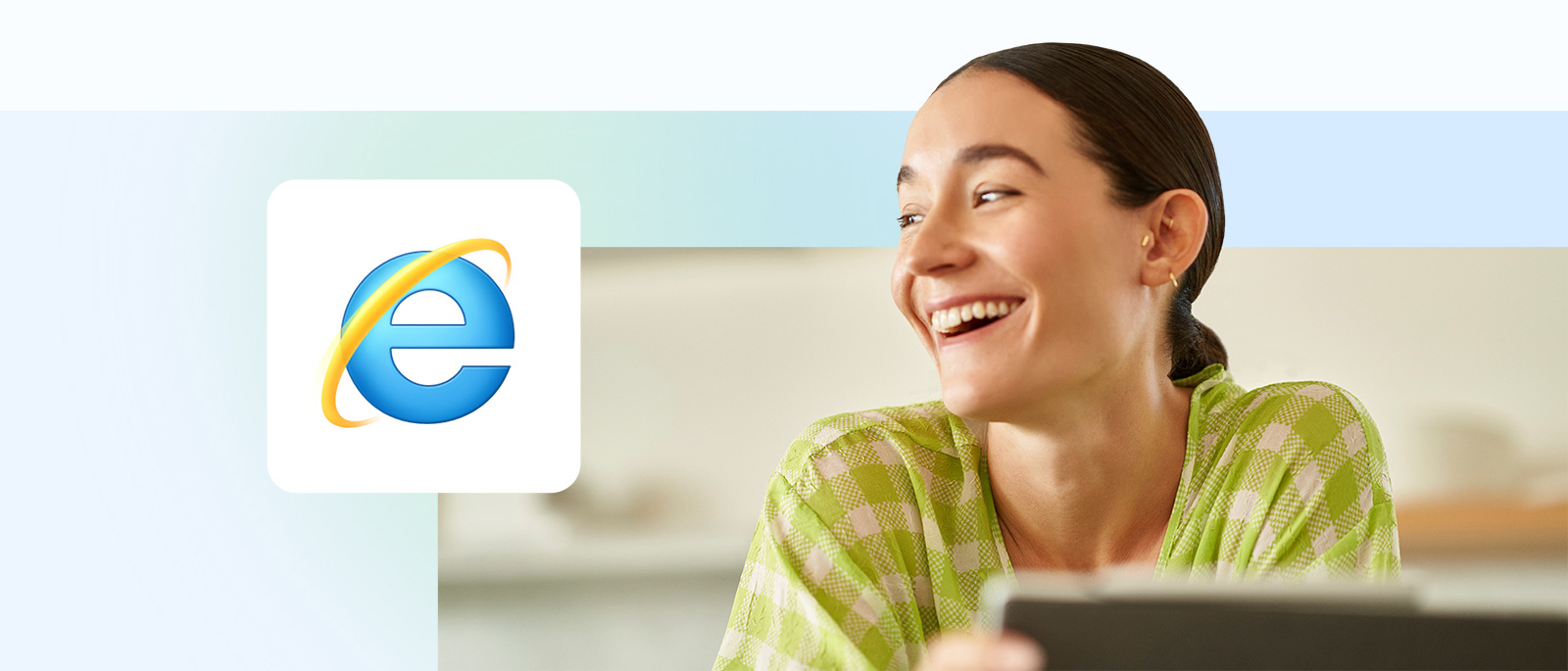 Internet Explorer アイコンが前面に表示されたノート PC の前に座って微笑む人。