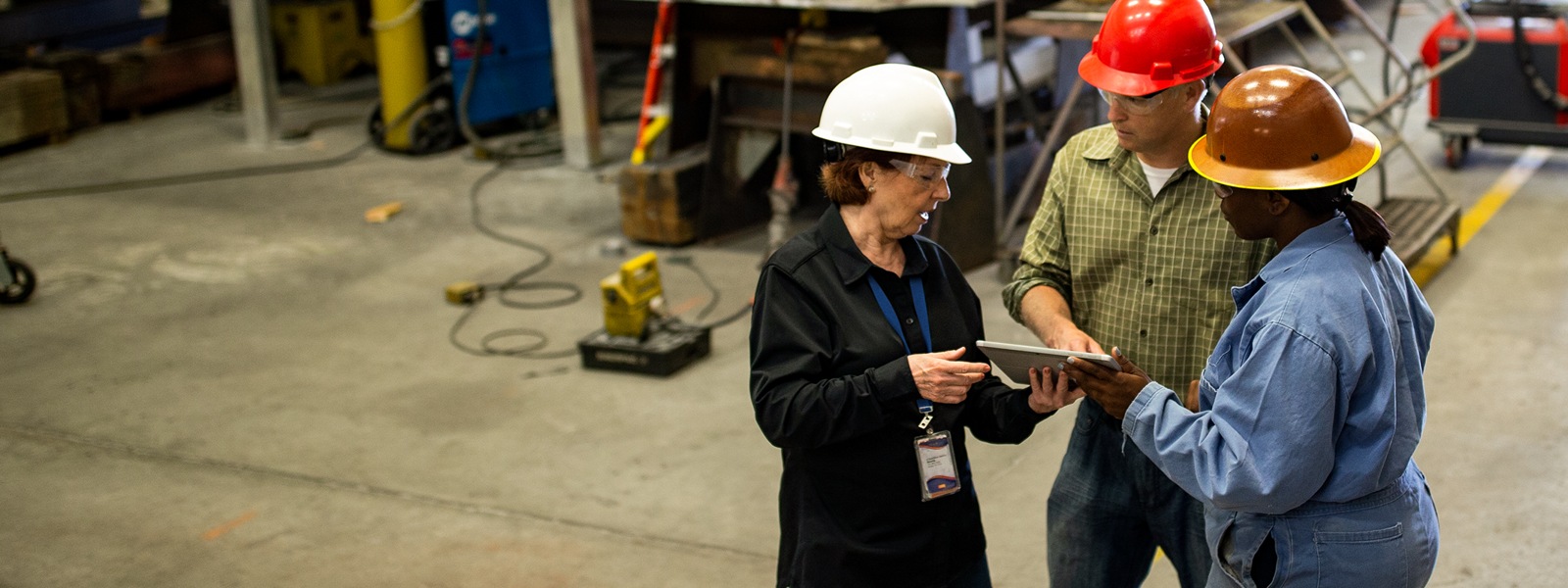 Three people in a manufacturing factory, standing together talking around a tablet