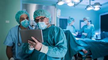 Two medical professionals in full scrubs in an operating room viewing information on tablet