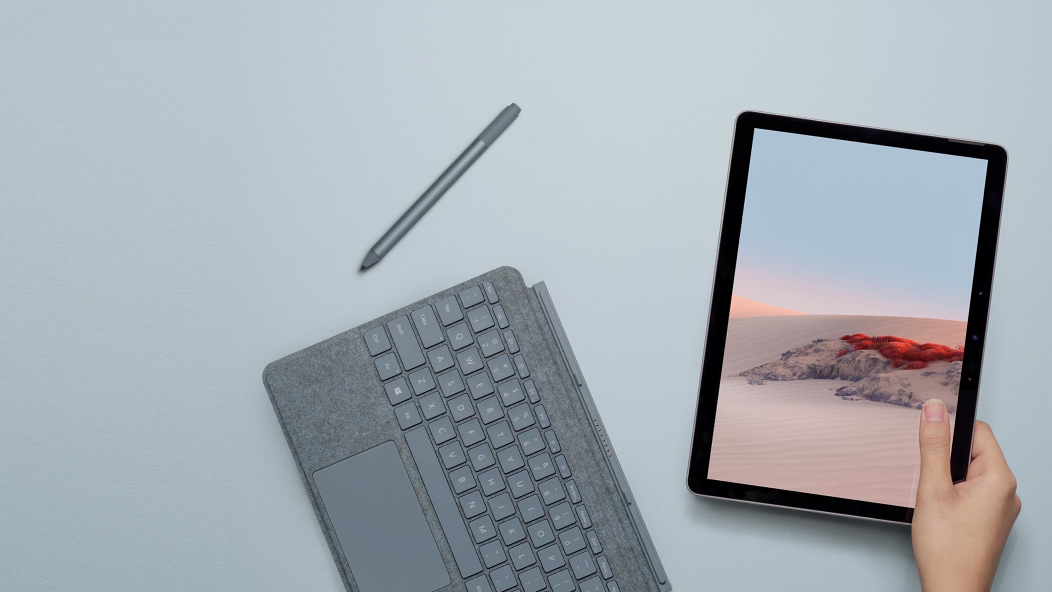 Une femme tient une Surface Go 2 à côté d’un clavier Type Cover et d’un stylet Surface
