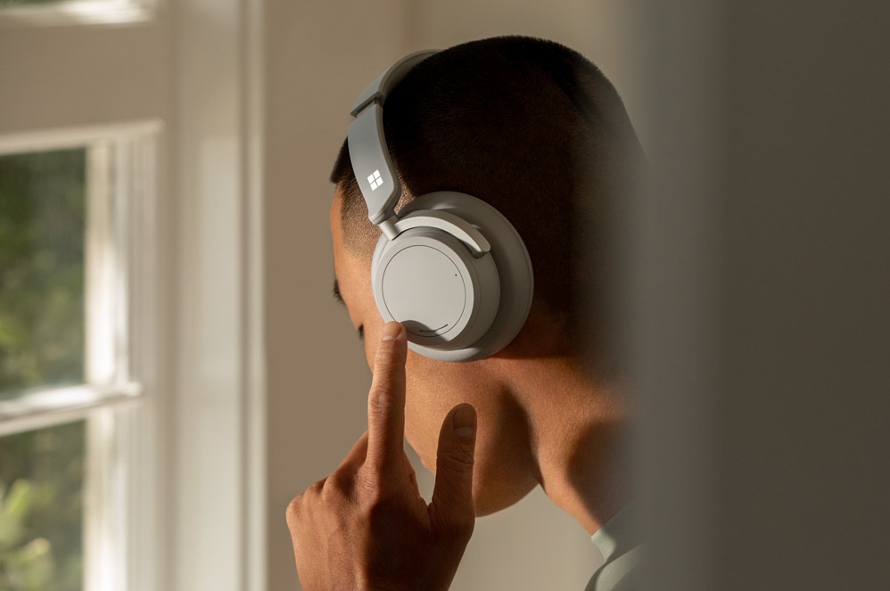 Een man gebruikt de linker on-ear-draaiknop om ruisonderdrukking op Headphones 2 aan te passen