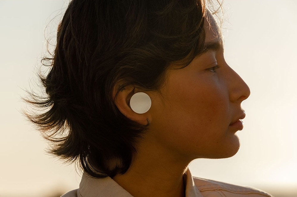 A woman wears Surface Earbuds while standing outside an office building.