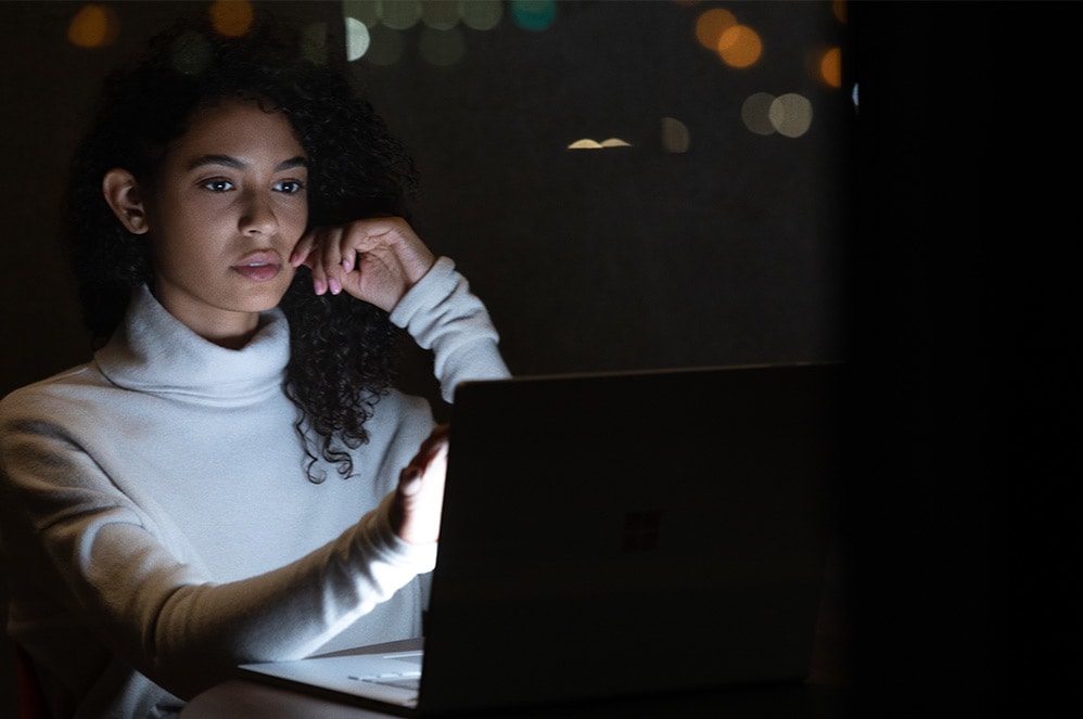 A woman works on her Surface Book 3 at the office late into the night