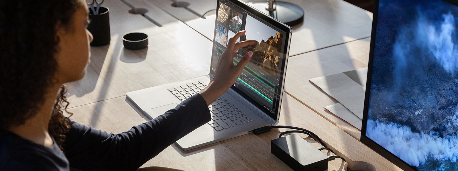 A woman interacts with Adobe Premier Pro on her Surface Book 3, which is connected to a 4K monitor on her desk