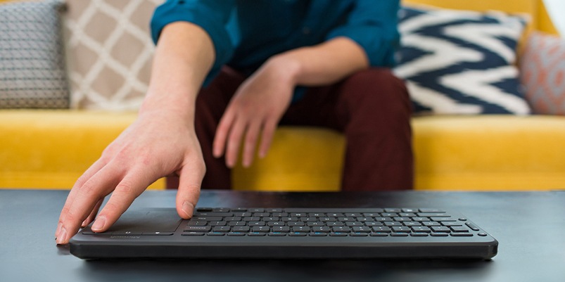 A person sitting on a couch uses a wireless Microsoft keyboard.