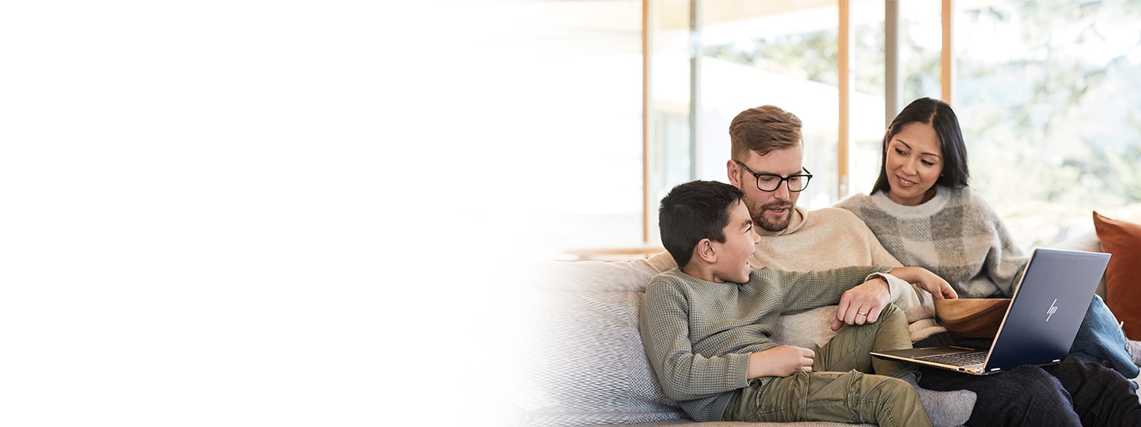Una madre, un padre e il loro bambino seduti su divano con un portatile Windows 10