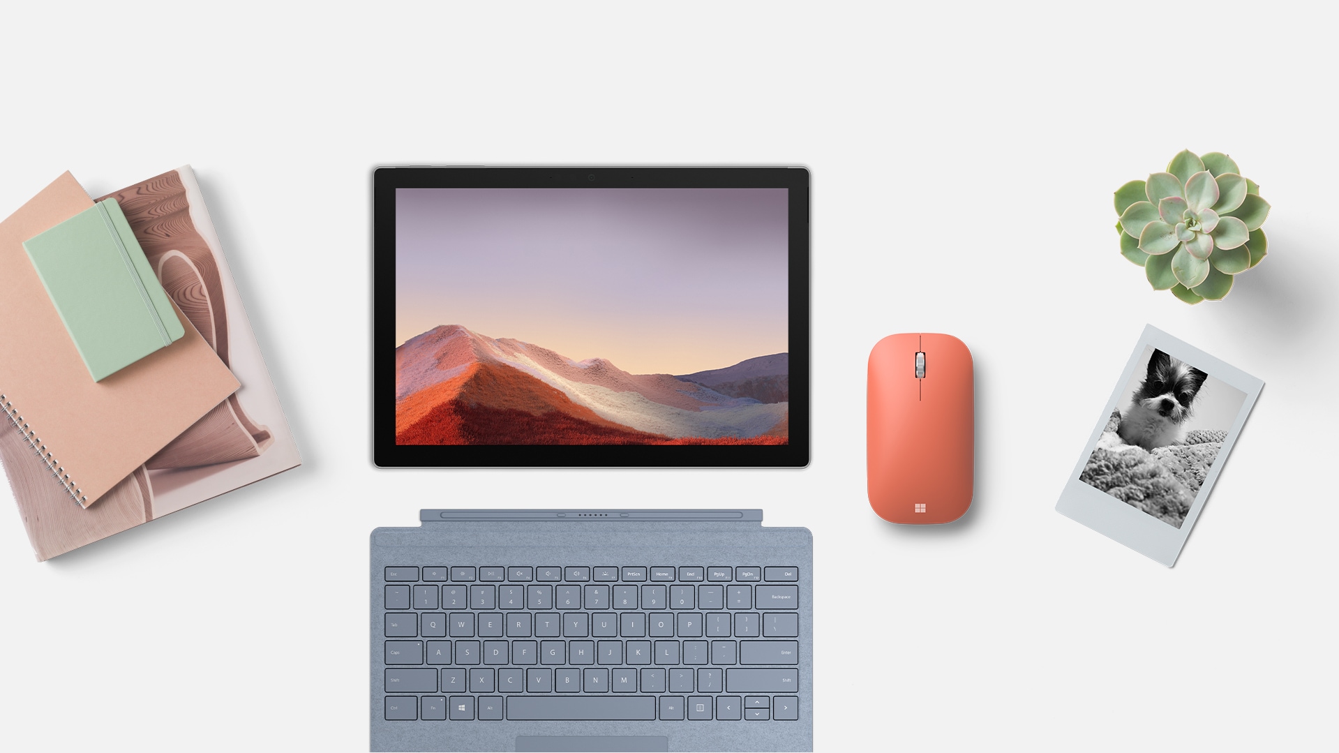 Un Microsoft Modern Mobile Mouse posé sur un bureau à côté d’une tablette, de plusieurs blocs-notes et d’une plante. 