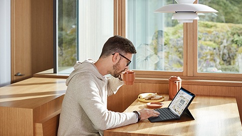 A man drinking coffee while working on his tablet