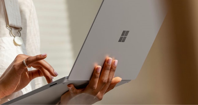 Close-up of a Surface laptop. One hand is holding the laptop as the other hand types on the keyboard.