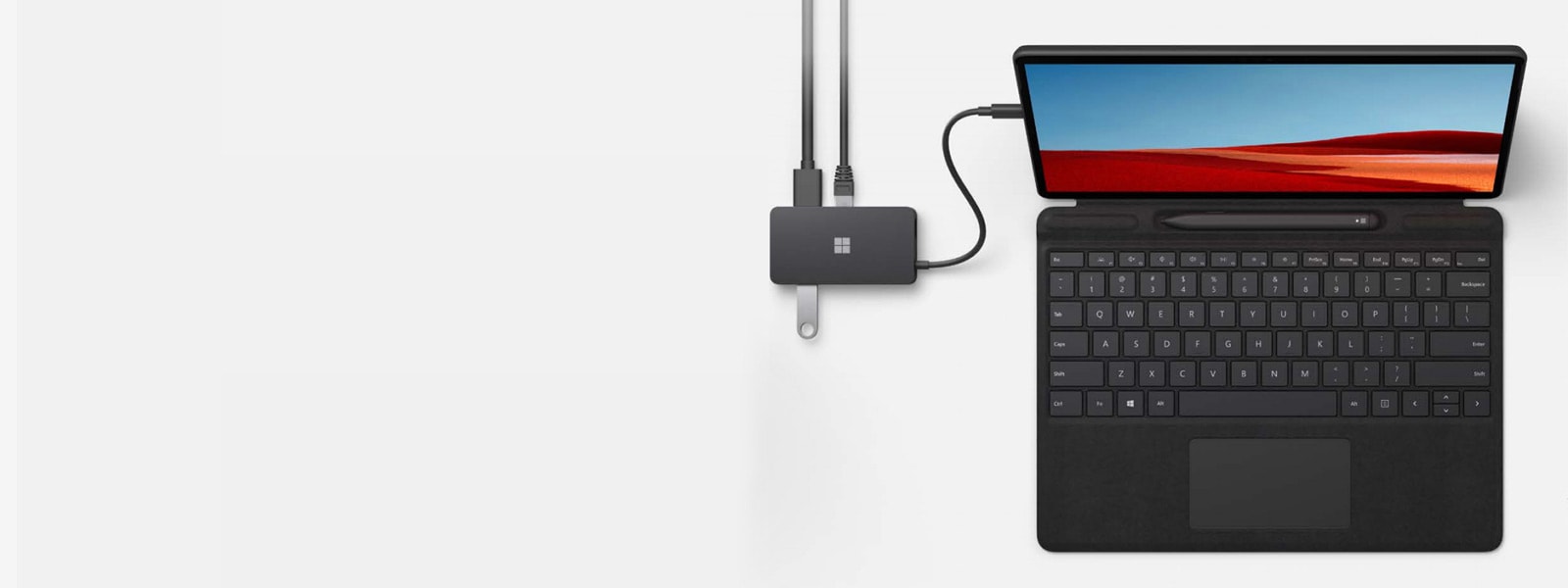 Ένας διανομέας ταξιδιού Microsoft USB-C® πάνω σε ένα γραφείο, συνδεδεμένος σε μια συσκευή Surface