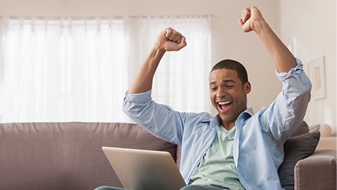 A man celebrating with his arms up while looking at his laptop computer