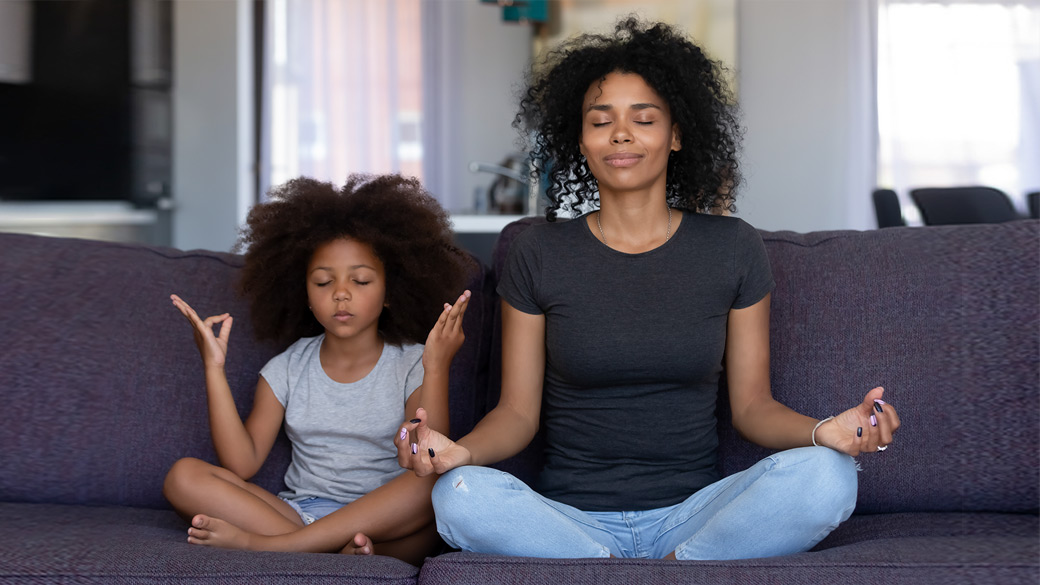 Photo credit: fizkes/iStock/Getty Images. Mother and young daughter doing yoga together at home on their couch.