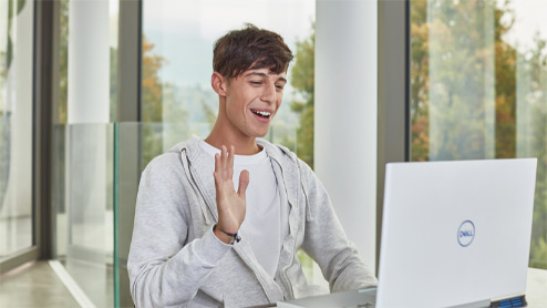 Sitting man smiles and waves at Windows 10 laptop.