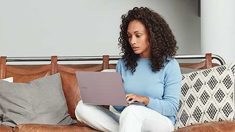 一名女性坐在沙发上，看着她腿上的笔记本电脑。