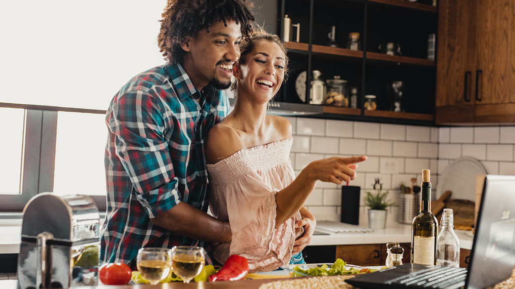 Photo credit: blackCAT/E+/Getty Images. Smiling man and woman look at recipe on Windows laptop while cooking together in kitchen