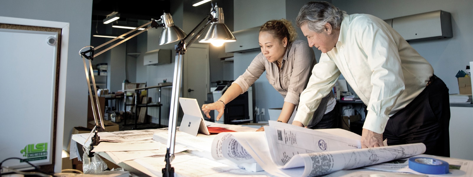 Two business professionals viewing architectural drawings on drafting table.
