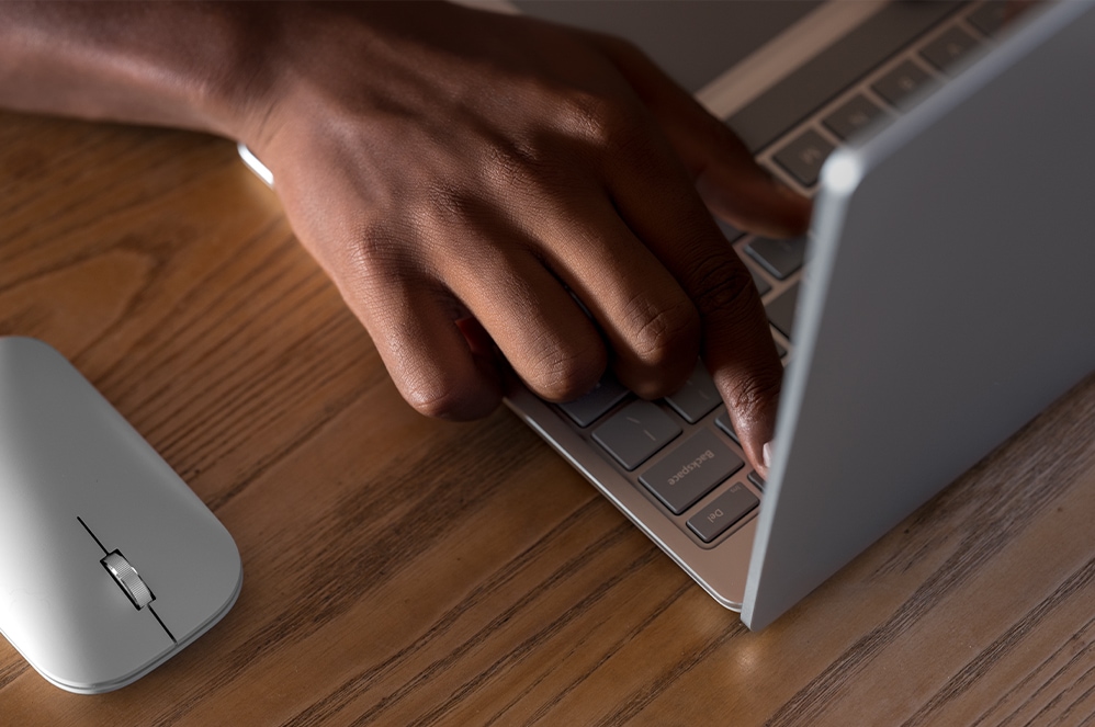 A person's hand typing on the Surface Laptop Go keyboard with a Surface Mobile Mouse nearby.