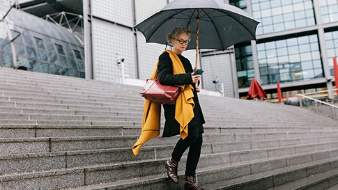 우산을 들고 야외 계단을 내려오면서 스마트폰을 확인하는 여성