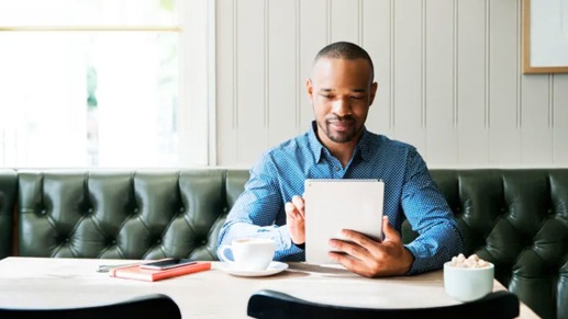 A person in a blue shirt sitting at a table looking at a tablet