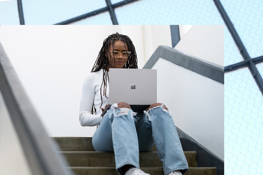 A woman works on her Platinum Surface Laptop 5 in a staircase.
