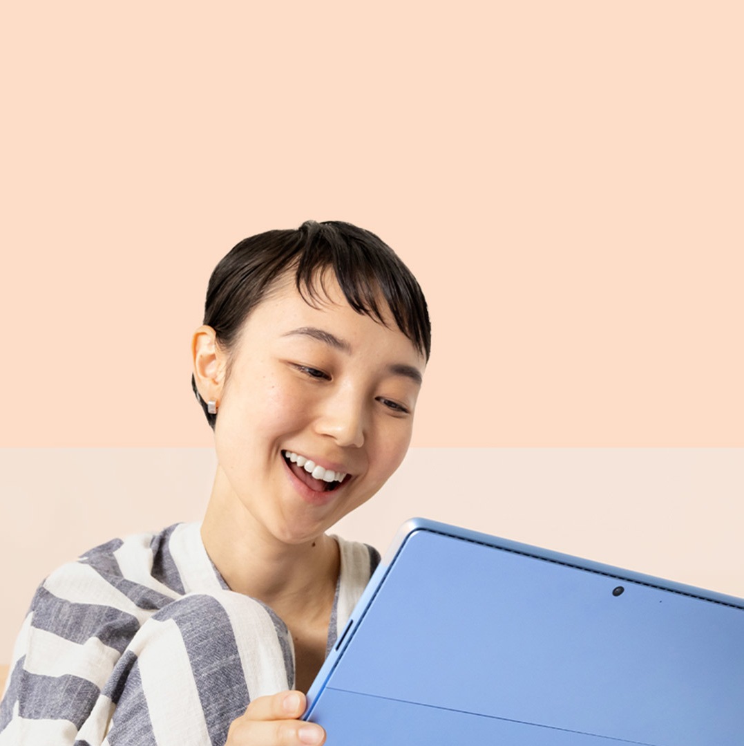 Una donna sorride davanti al suo dispositivo Surface Pro 9 nel colore Zaffiro e tiene una penna Surface Slim Pen 2.