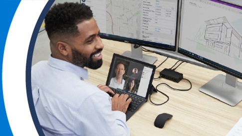 Ein Mann sitzt lächelnd am Schreibtisch mit Laptop und zwei Bildschirm vor sich.